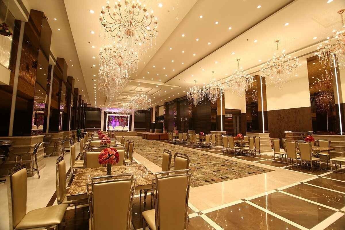 A large, elegant banquet hall with crystal chandeliers hanging from a high ceiling, round dining tables.