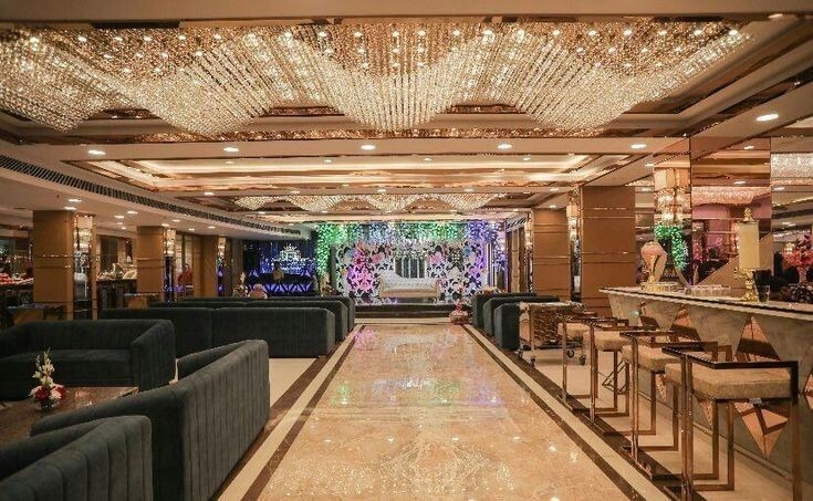 Modern banquet hall with crystal ceiling lights, stylish seating arrangement, and decorated stage for wedding or reception.