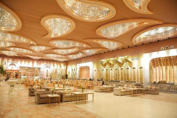 Spacious wedding banquet hall with golden interiors, designer ceiling lights, and comfortable sofa seating arrangement for grand events.
