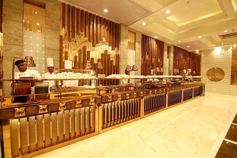 A luxurious buffet counter inside a banquet hall with chefs serving food behind a long golden food station.