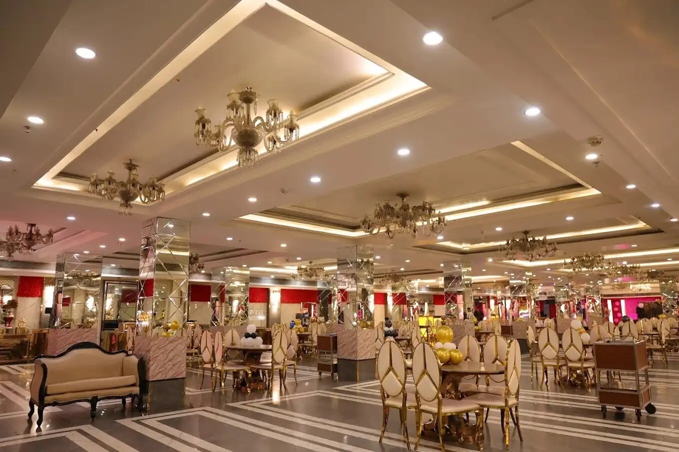 Elegant banquet hall with mirrored pillars, chandeliers, gold chairs, and round tables arranged for a wedding or celebration event.